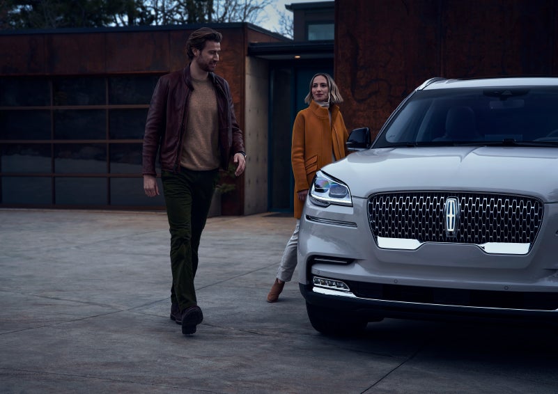 A man and a woman approaching a 2024 Lincoln Aviator® SUV, which illuminates certain lights when they are close | Mike Reichenbach Lincoln in Florence SC